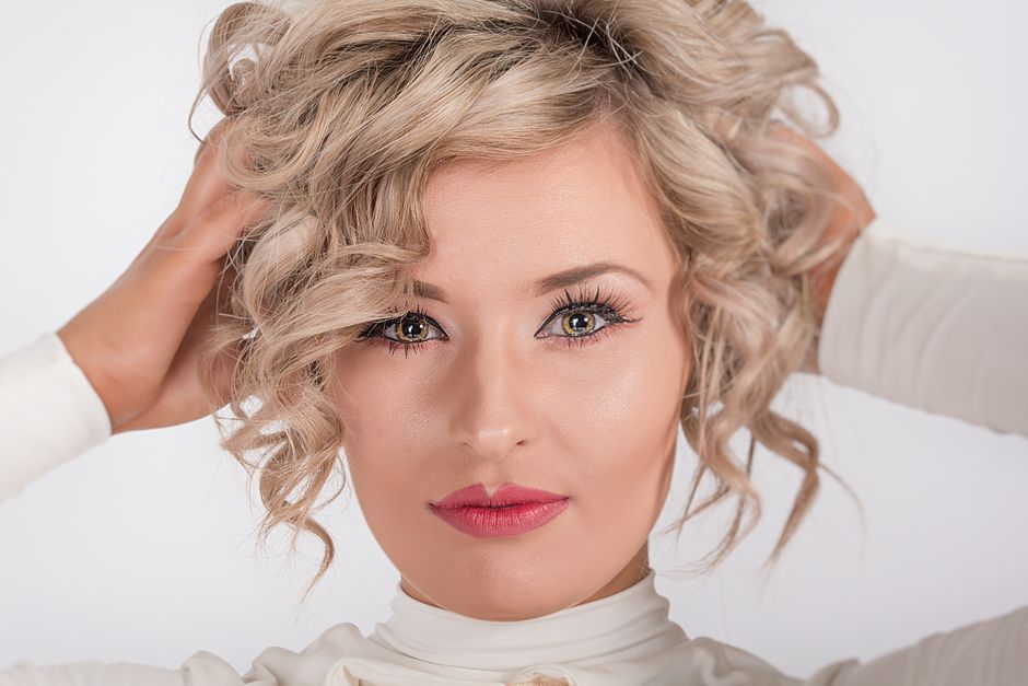 Close-up portrait of a blonde woman with curly hair and makeup, embracing elegance.