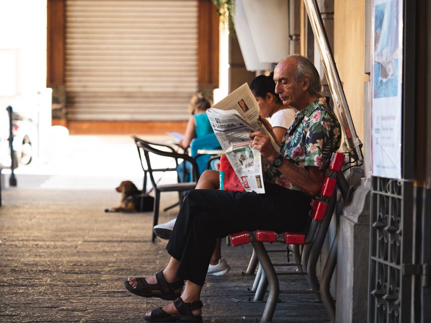 A senior man reads a newspaper sitting in an outdoor café, creating a relaxing street scene.