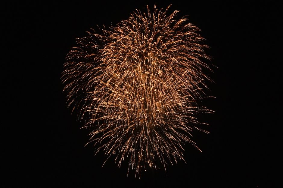 Bright golden fireworks explode against a black night backdrop, lighting up the sky.