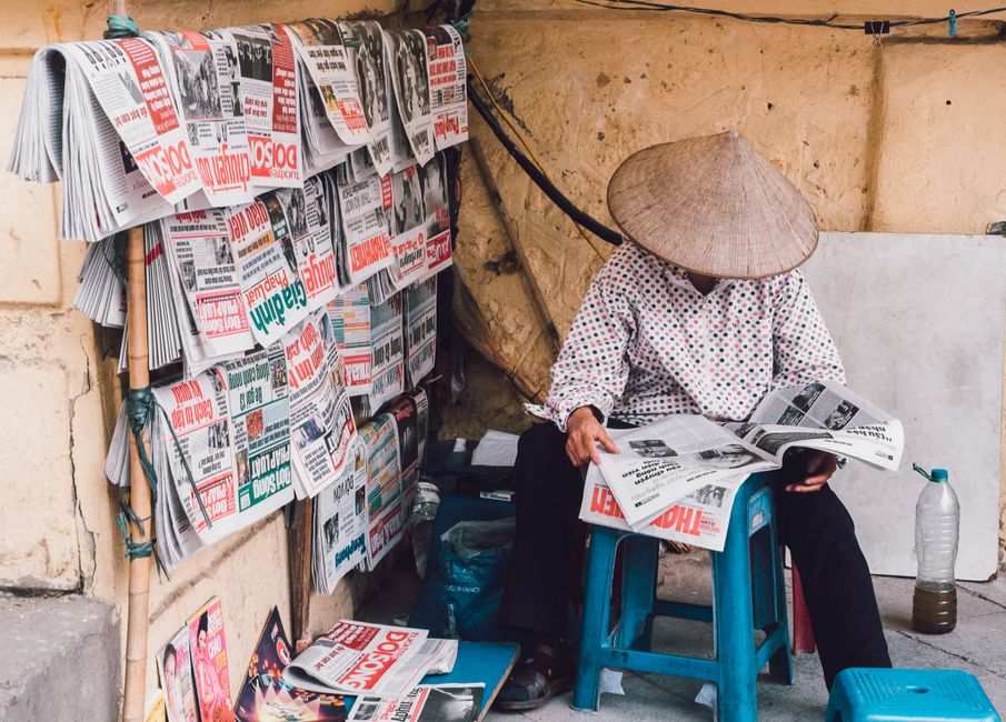 A street vendor in Hanoi reads newspapers, showcasing daily life in Vietnam.