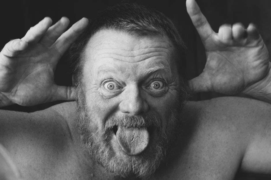 Black and white portrait of a senior man making a goofy face, sticking out his tongue.