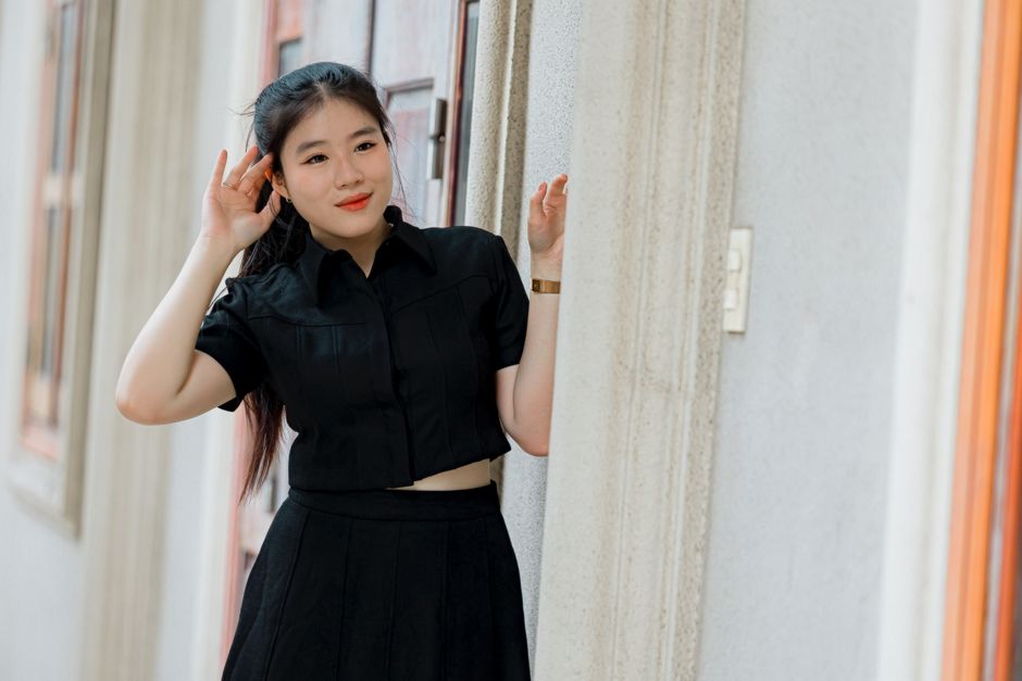 Confident young woman in black dress posing casually outside a building.