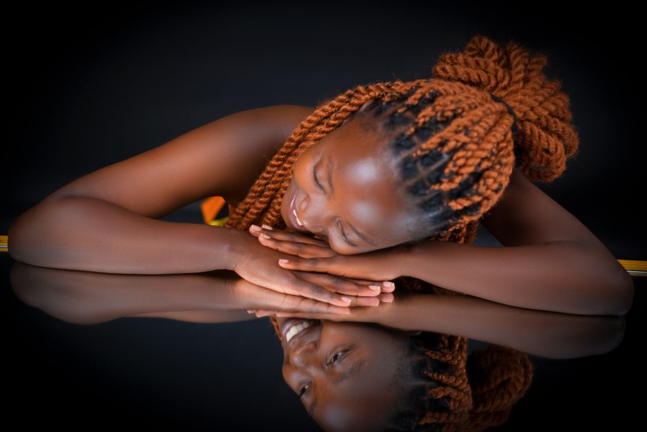 An artistic portrait of a woman with braided hair reflecting on a shiny surface.