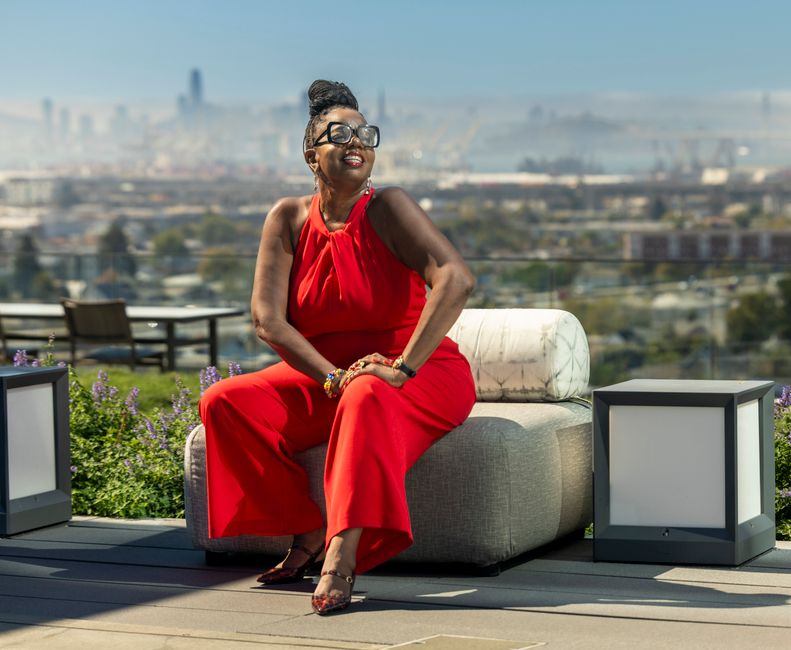 Stylish woman in red enjoying a sunny day with a cityscape background, radiating joy and confidence.