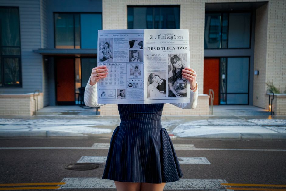 A stylish woman reading a newspaper in a winter urban environment, showcasing street fashion.