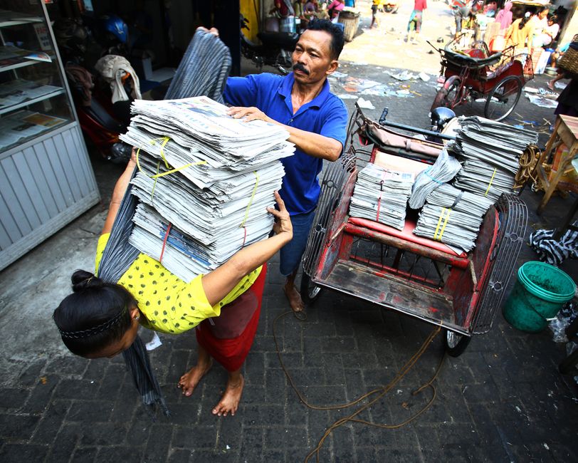 Street vendors transferring newspapers on a busy street in Surakarta, Indonesia, showcasing local hustle.
