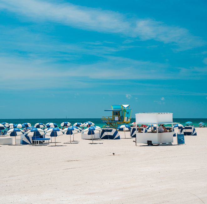 A vibrant beach scene featuring blue umbrellas and a colorful lifeguard tower on a sunny day.