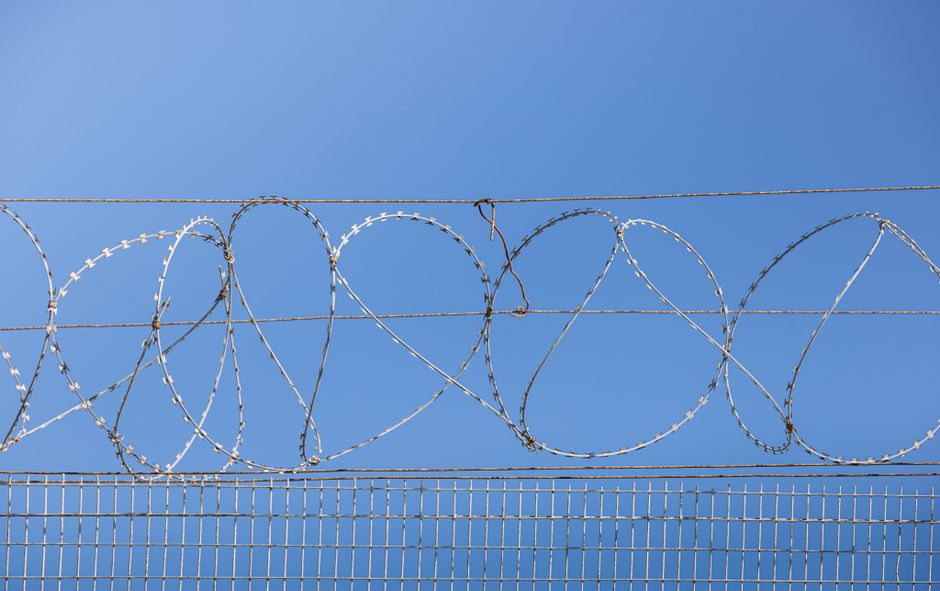 Detailed image of barbed wire fence under clear blue sky, symbolizing security and restriction.