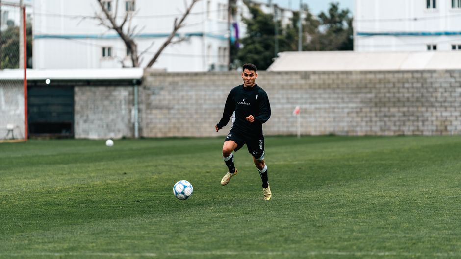 Energetic young male soccer player dribbling on a grassy field during the day.