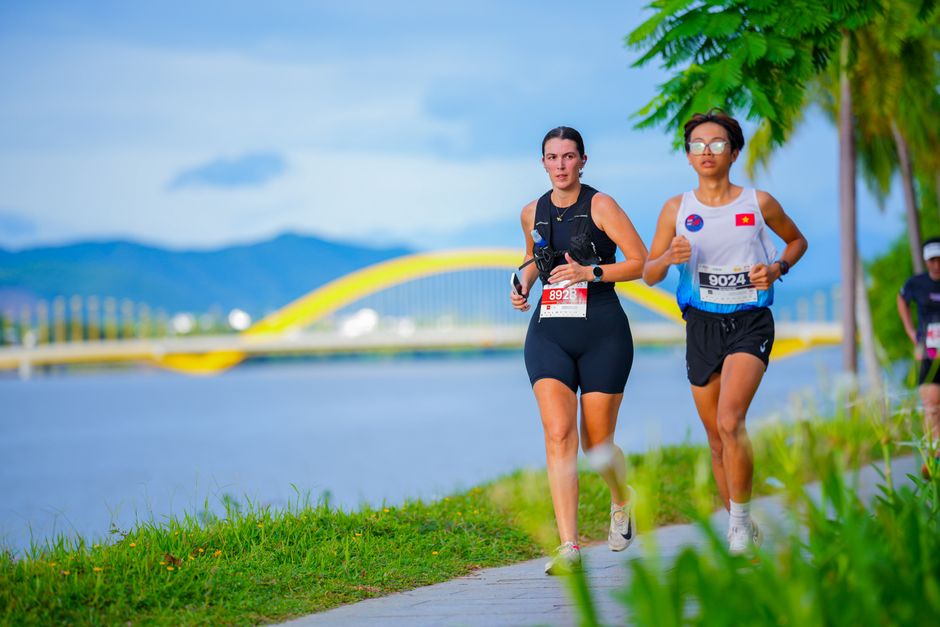 Two women jogging near the iconic Dragon Bridge in Da Nang during a marathon event.