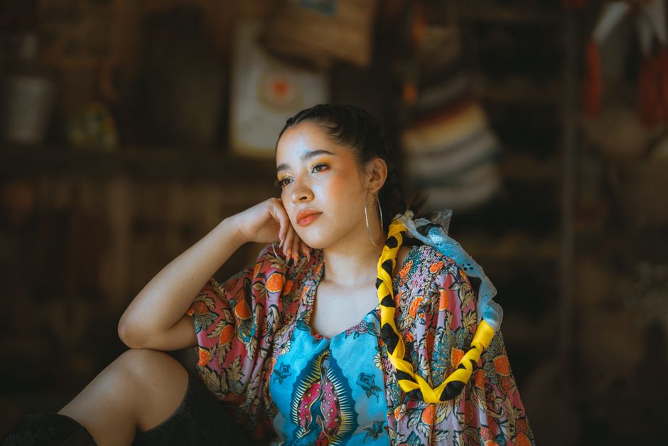 A young woman in vibrant traditional clothing poses indoors, embracing her cultural heritage.