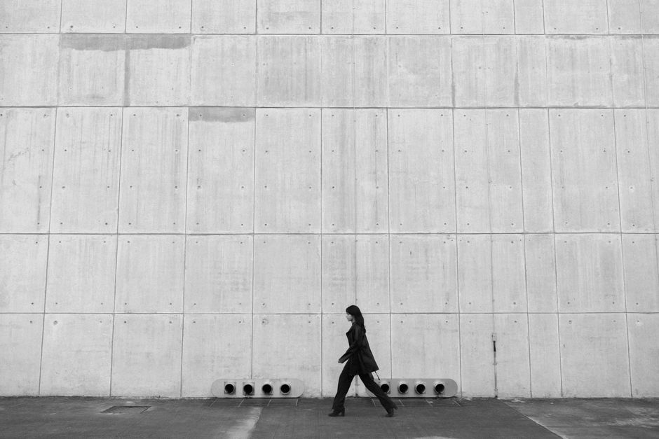 Black and white photo of an individual walking alongside a minimalist concrete wall.