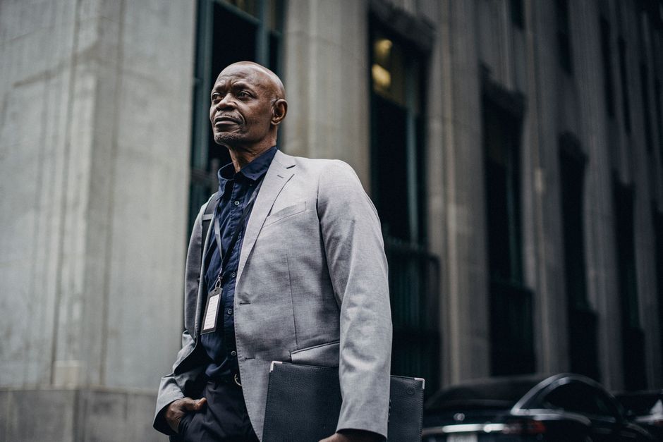 Concentrated adult African American businessman wearing classy formal suit standing with hand in pocket against modern building in urban environment and looking away pensively