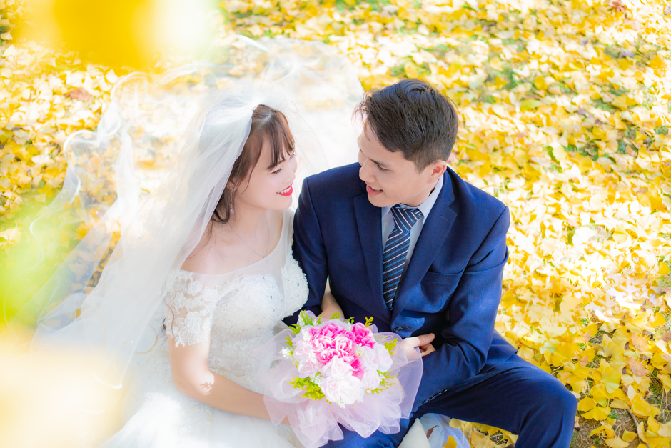 Bride and groom celebrate in a park surrounded by vibrant ginkgo leaves in autumn.