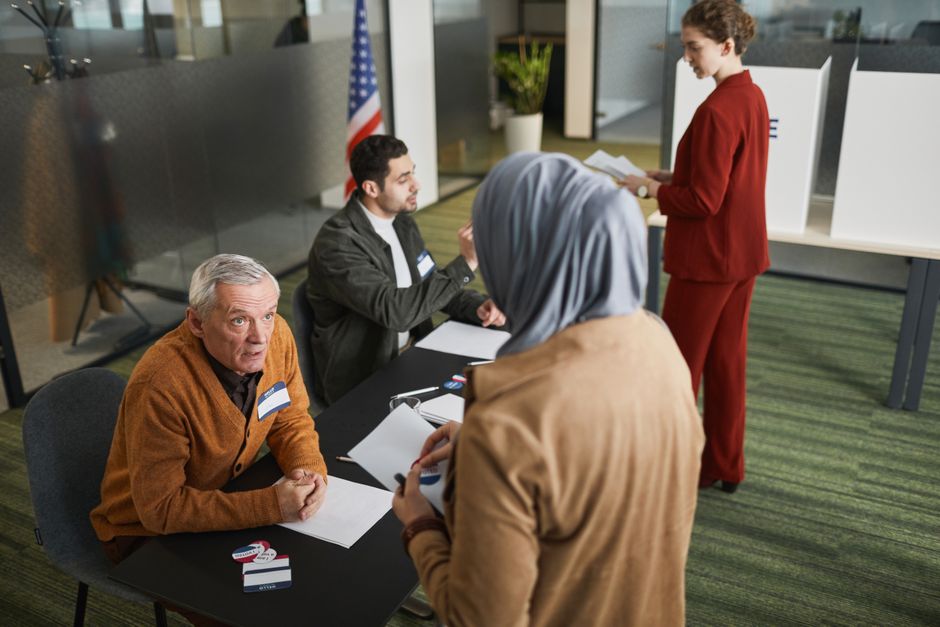 Adults engaging in the voting process at an indoor polling station, representing diverse backgrounds and social responsibility.