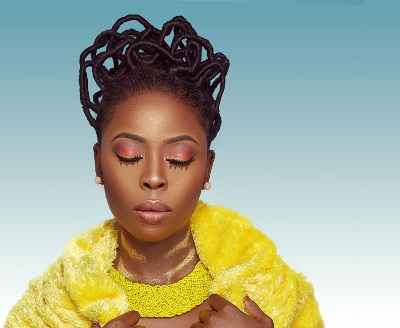 Stunning portrait of an African woman showcasing her glamorous makeup and stylish yellow fur coat against a blue background.