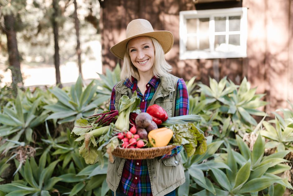 Woman in garden holding a basket of fresh organic vegetables with greenery in the background.