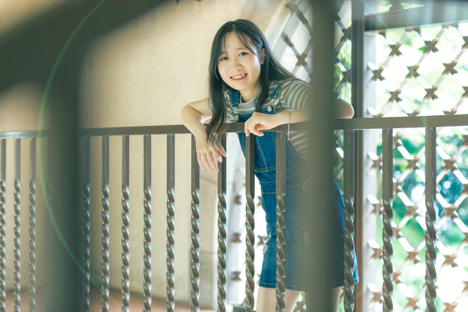 A cheerful young woman leaning on a balcony railing, enjoying the sunny day.