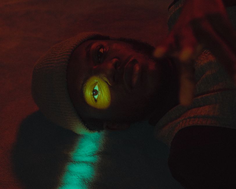 Artistic close-up of a person lying in a dark room with colorful lighting.