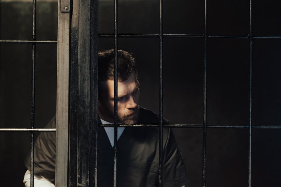 A man with a somber expression behind bars, symbolizing confinement and introspection.