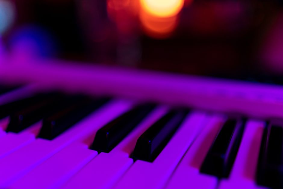 A focused close-up of piano keys with vibrant pink and purple lighting, creating a moody atmosphere.