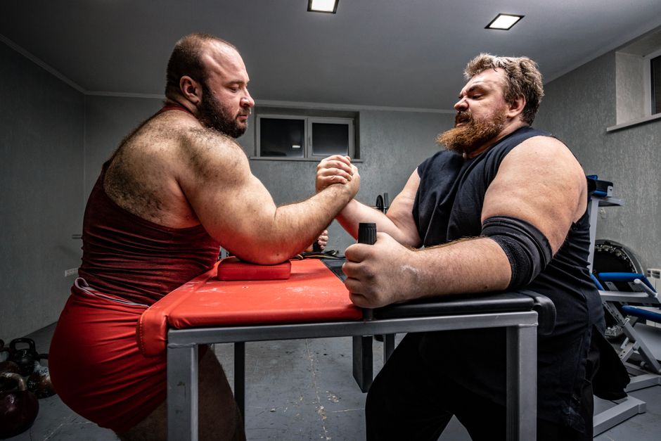 Two muscular men in a gym engage in a face-to-face arm wrestling match.