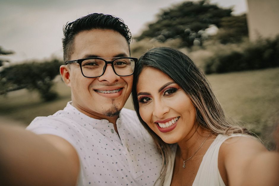 Happy couple smiling for a selfie in a natural outdoor setting, capturing a joyful moment together.