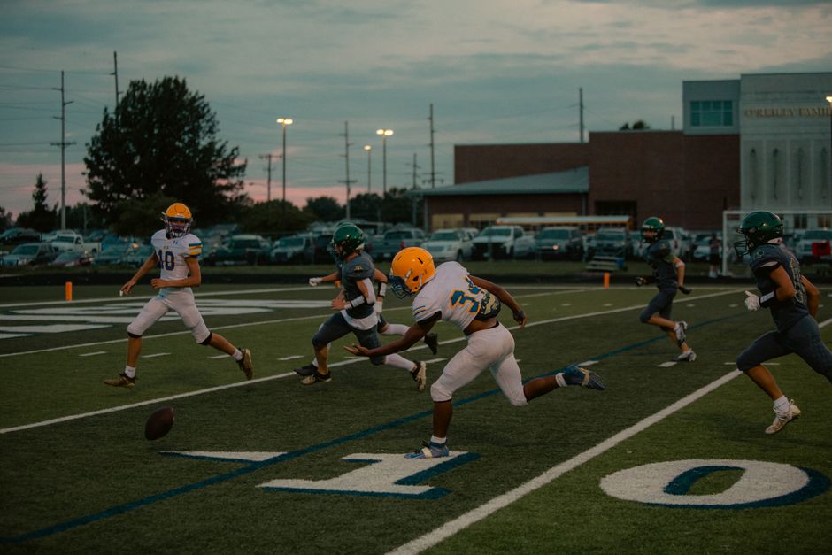 Football players in action during an evening high school game with dramatic sky backdrop.