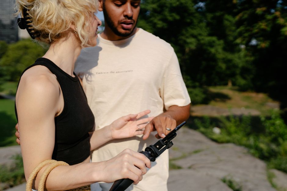 A diverse couple examines a phone on a tripod outdoors, enjoying a sunny day.