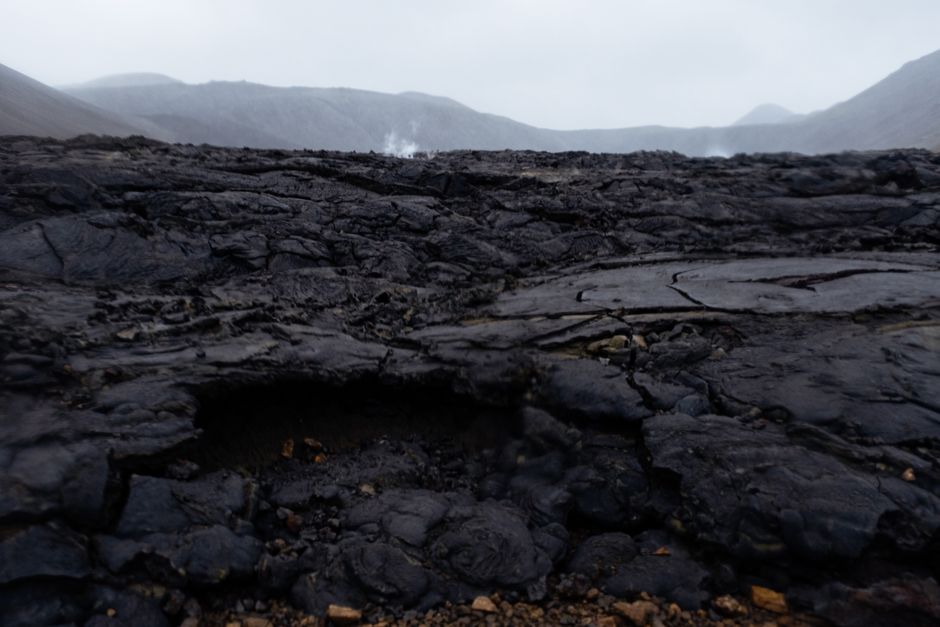 Captivating view of a rugged, cracked lava field with steam rising in the background, showcasing geological beauty.
