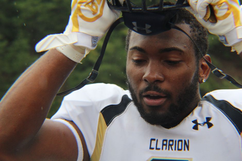 Close-up of a football player adjusting his helmet mid-game, showcasing focus and athleticism.