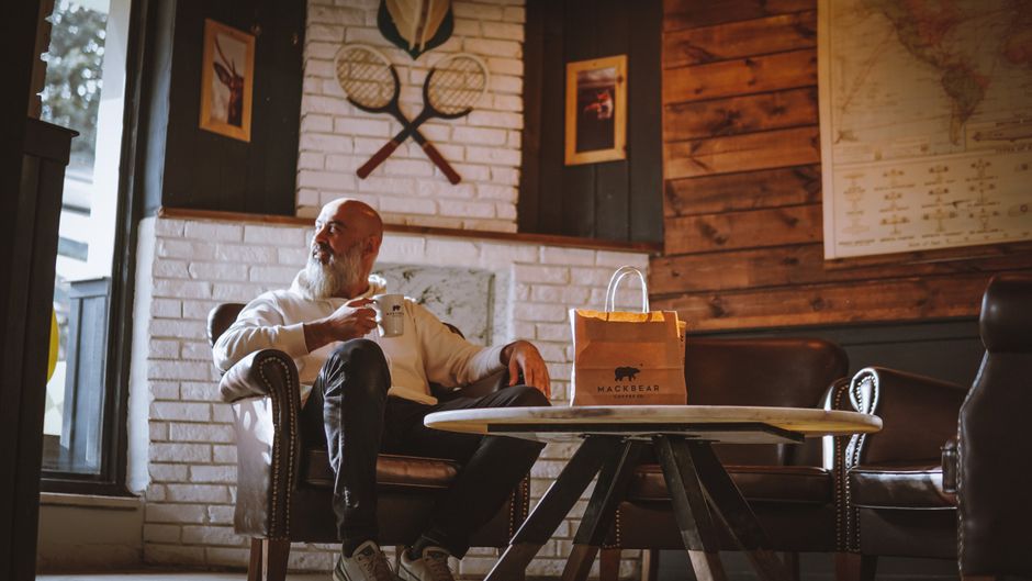 Bearded man enjoying coffee in a rustic cafe setting, with vintage decor and warm ambiance.