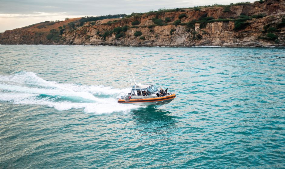 A speedboat glides on turquoise ocean waters near rugged cliffs on a sunny day.