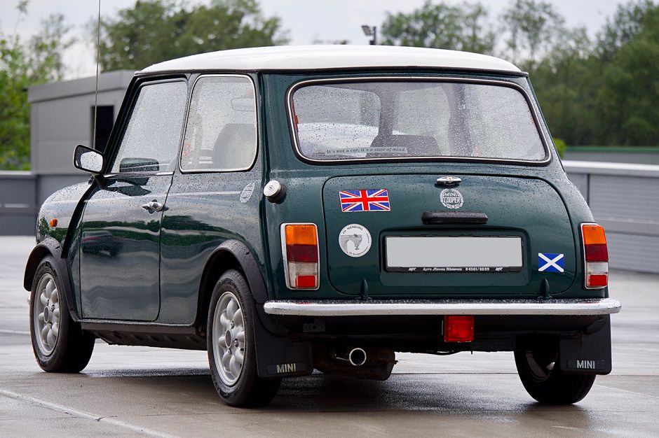 Rear view of a classic green Mini Cooper adorned with raindrops in an urban setting.
