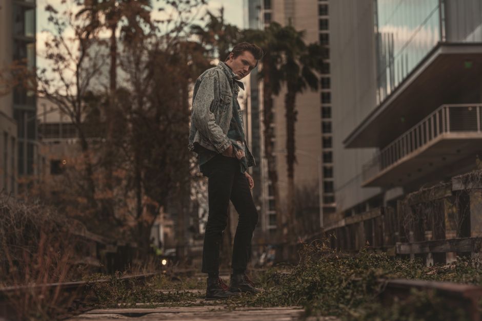 Stylish young man posing confidently on train tracks in an urban setting.