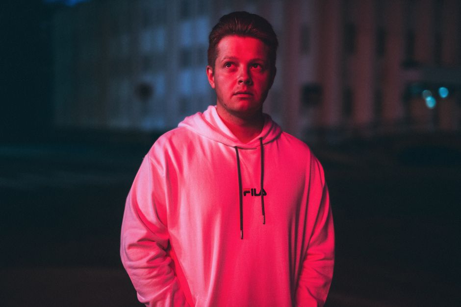 Portrait of a young man illuminated by vibrant pink light in an urban setting at night.
