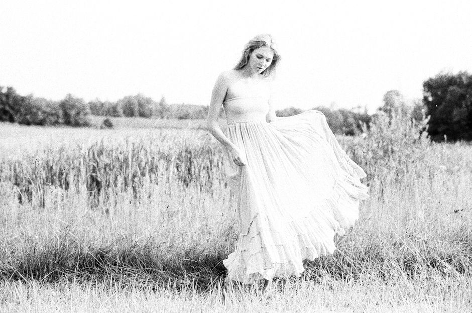 A woman poses gracefully in a strapless dress in a serene countryside setting.