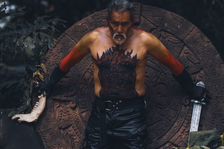 A tribal warrior with intricate body paint holding a sword against an ancient stone backdrop.