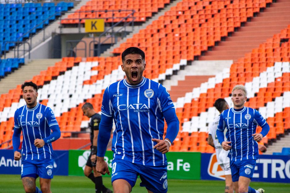 Soccer players in blue jerseys celebrate scoring a goal in an empty stadium.