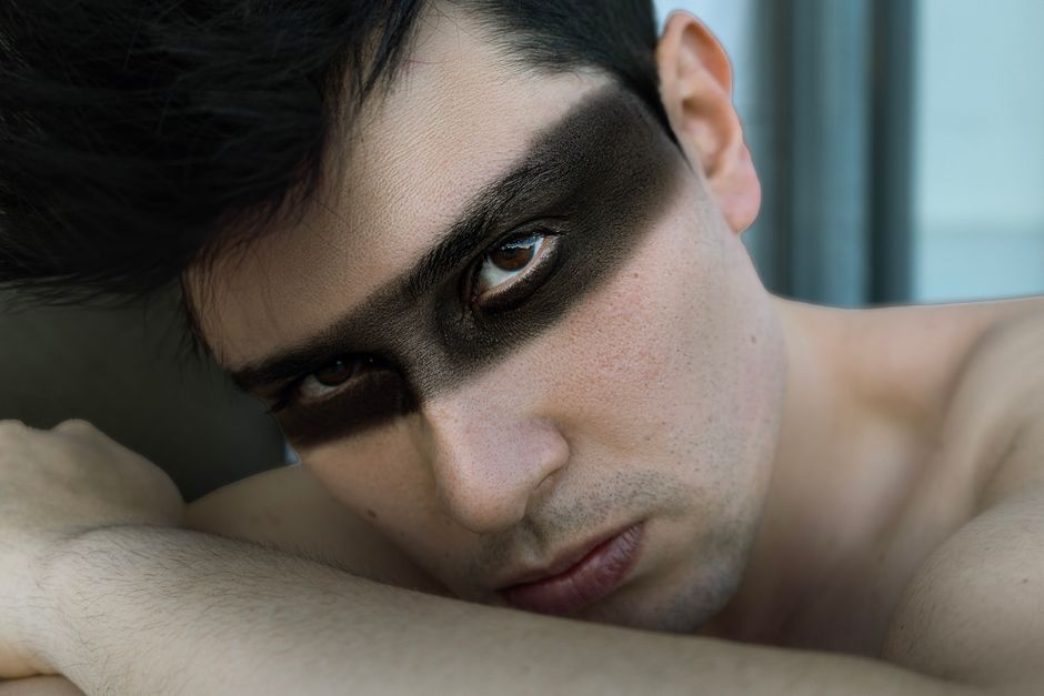 Close-up portrait of a young man with striking black eye makeup creating a bold and dramatic look.