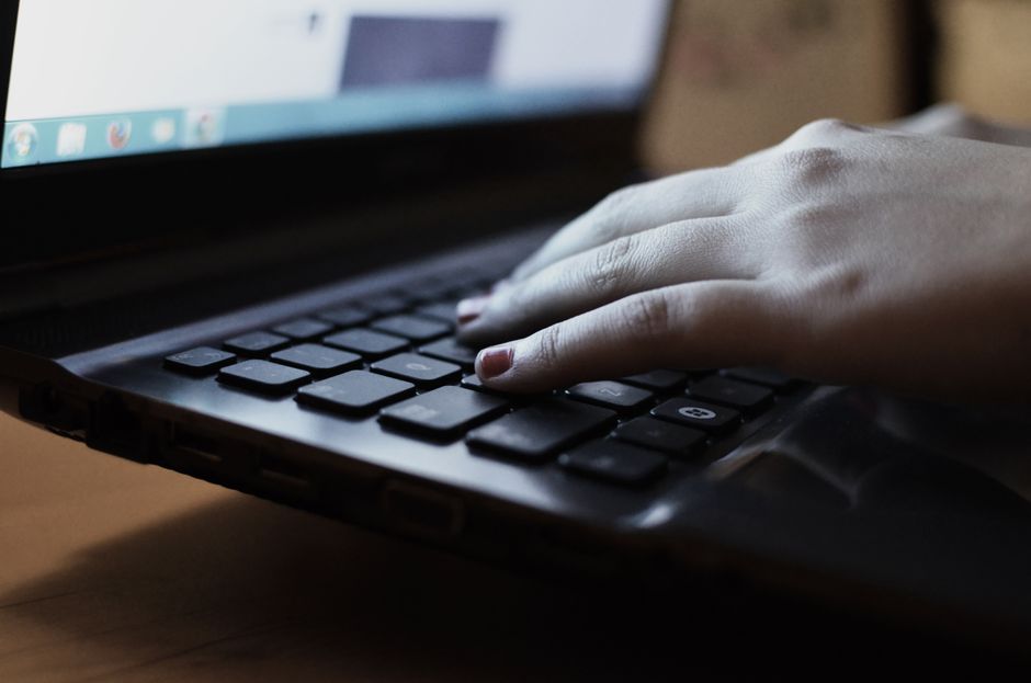 A close-up view of a person typing on a laptop keyboard indoors.
