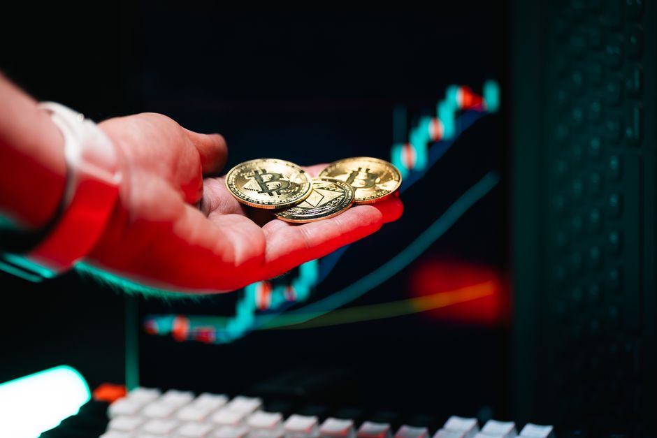 Close-up of hand holding cryptocurrency coins with trading chart in background.