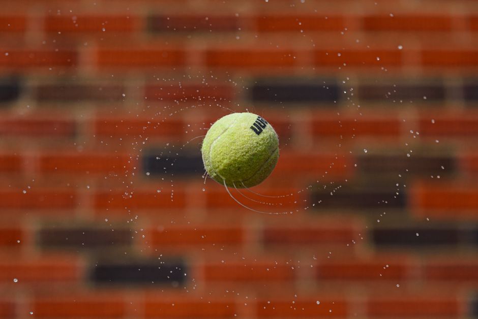 Dynamic shot of a tennis ball with water droplets against a brick wall.