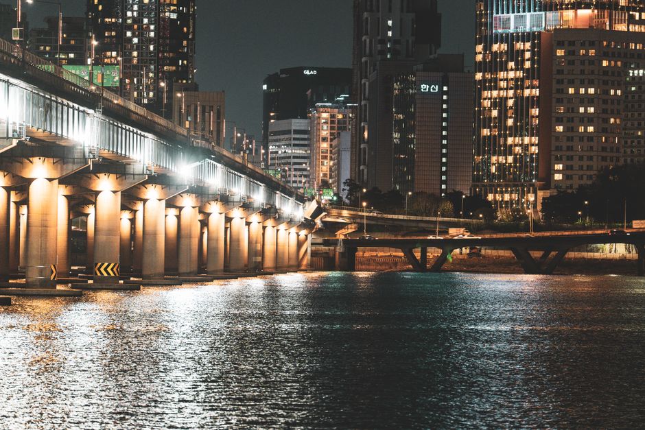 A city skyline at night with a beautifully lit bridge reflecting on water.