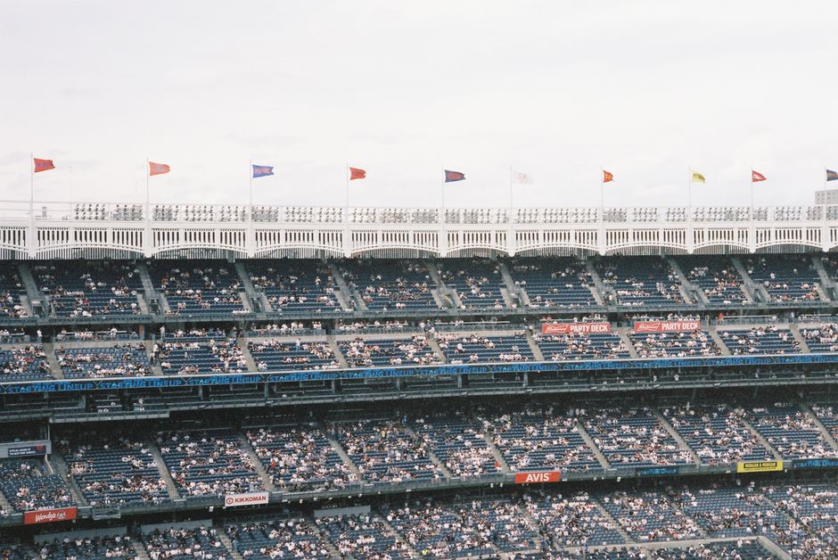 Crowd at Yankee Stadium watching a baseball game, flags waving atop tiers.