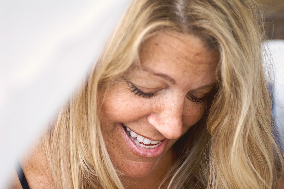 A woman with long blonde hair smiles warmly with eyes closed, radiating joy and contentment.