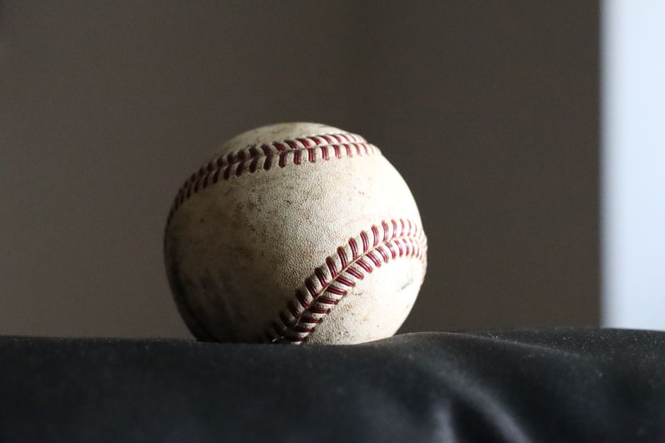High-resolution image of a worn baseball on a dark surface, highlighting its stitching and texture.