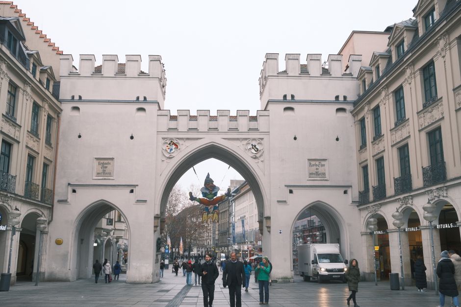 View of Karlstor gate in Munich with people walking along the street on a cloudy day.