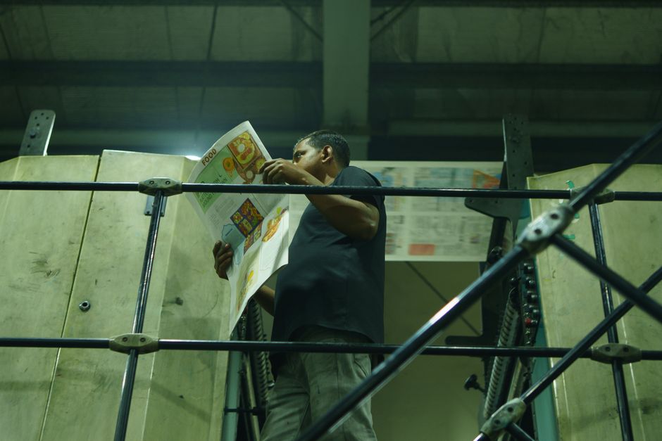 Man examines printed newspaper in an industrial printing environment with machinery.