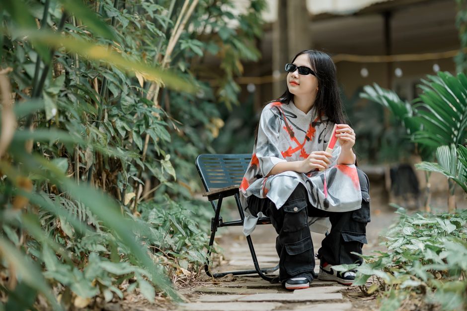 Woman in trendy attire enjoying a serene moment on a garden bench outdoors.